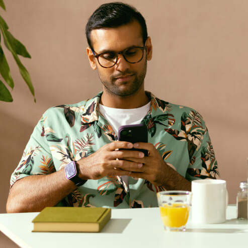Seorang pria duduk di meja di sebuah kafe, memeriksa akun Wise-nya menggunakan aplikasi ponsel pintar.